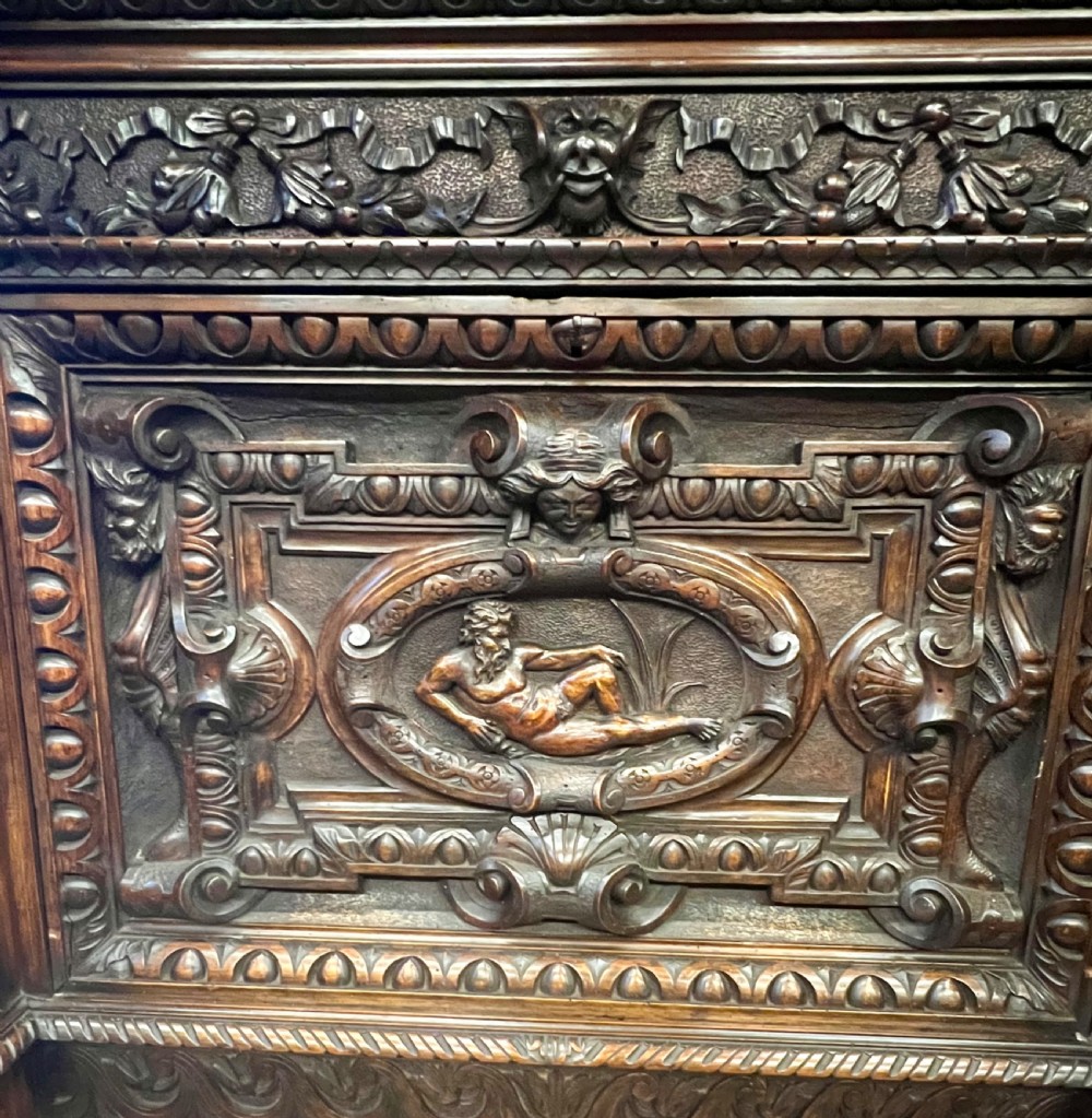 A heavily carved dark walnut cabinet featuring figurative reliefs, caryatid supports, mask motifs, and an architectural cresting. View XI