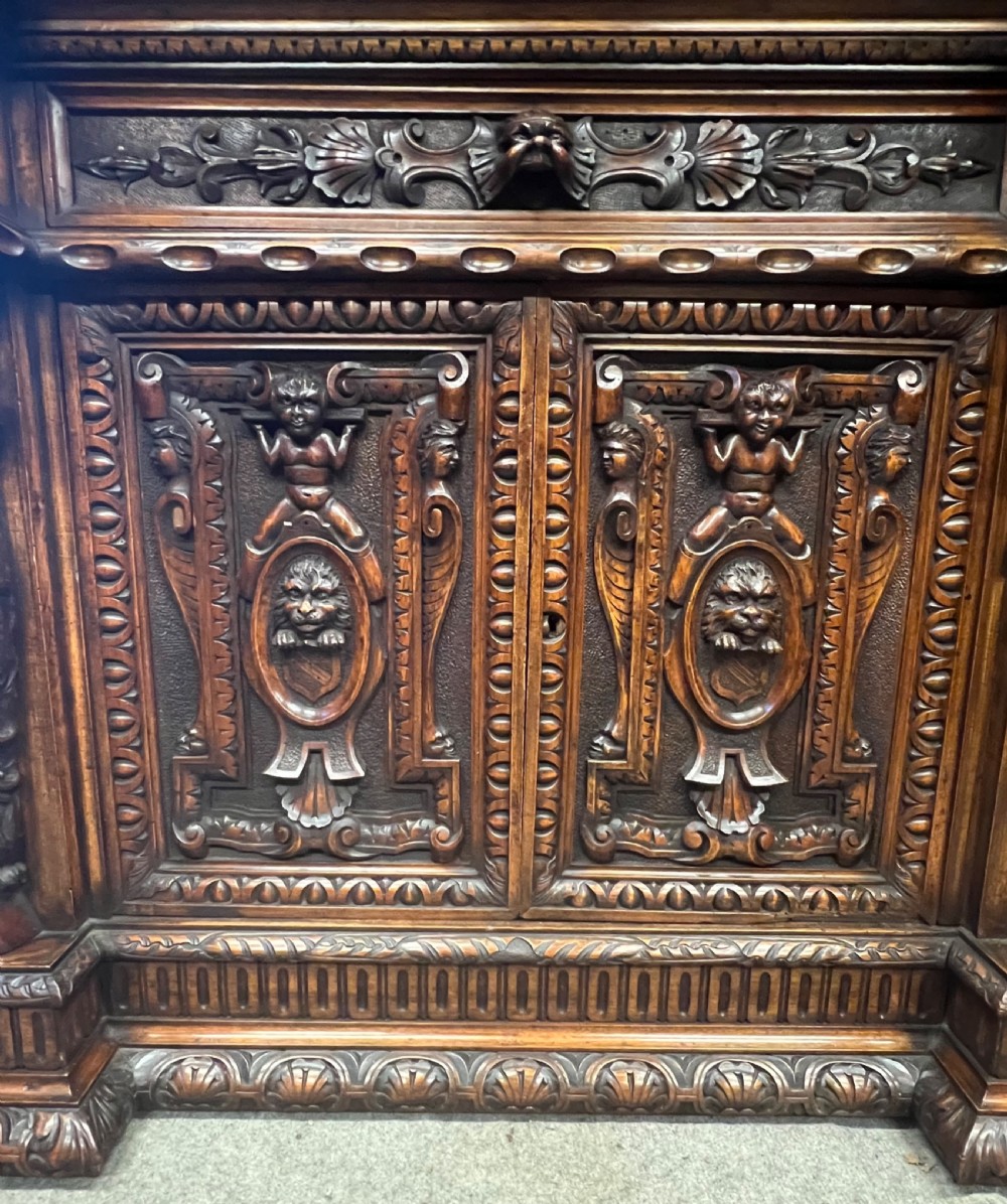 A heavily carved dark walnut cabinet featuring figurative reliefs, caryatid supports, mask motifs, and an architectural cresting. View XIII