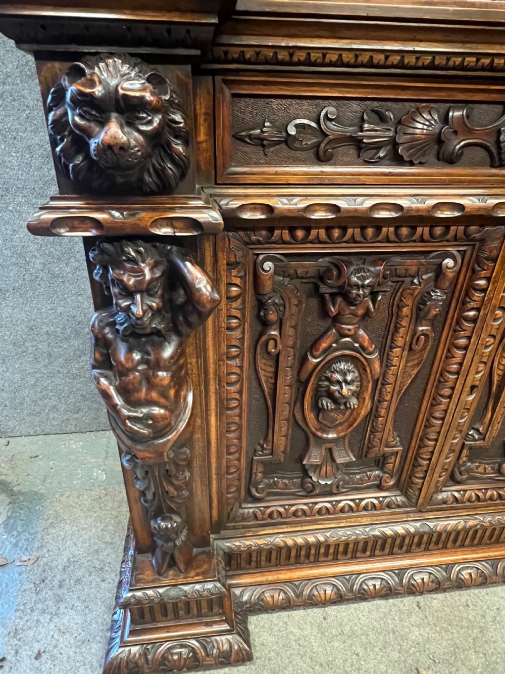 A heavily carved dark walnut cabinet featuring figurative reliefs, caryatid supports, mask motifs, and an architectural cresting. View XIV