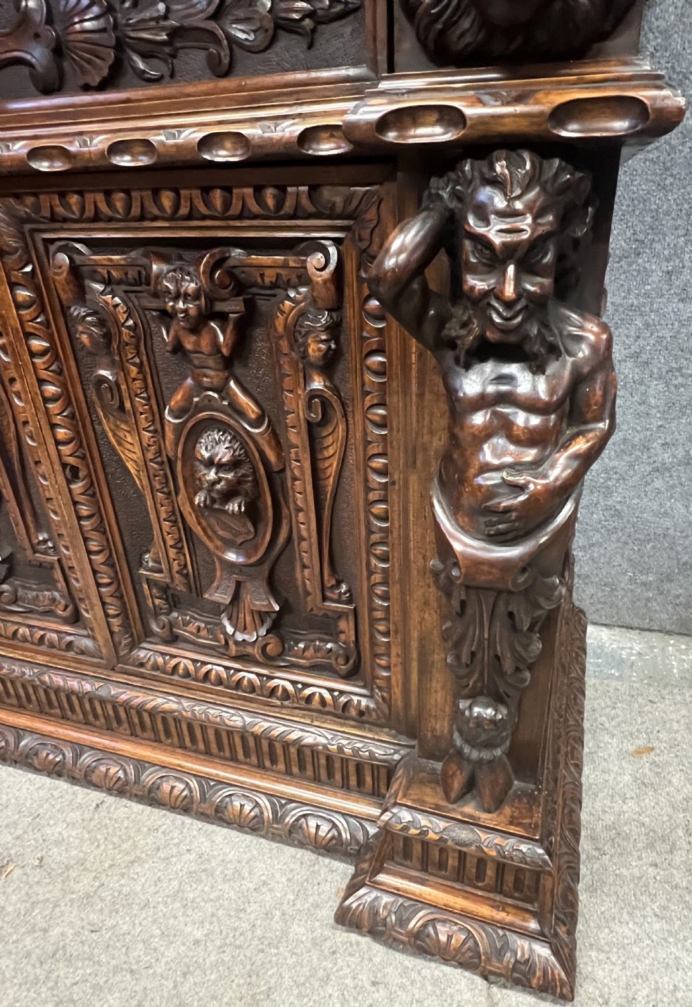 A heavily carved dark walnut cabinet featuring figurative reliefs, caryatid supports, mask motifs, and an architectural cresting. View XV