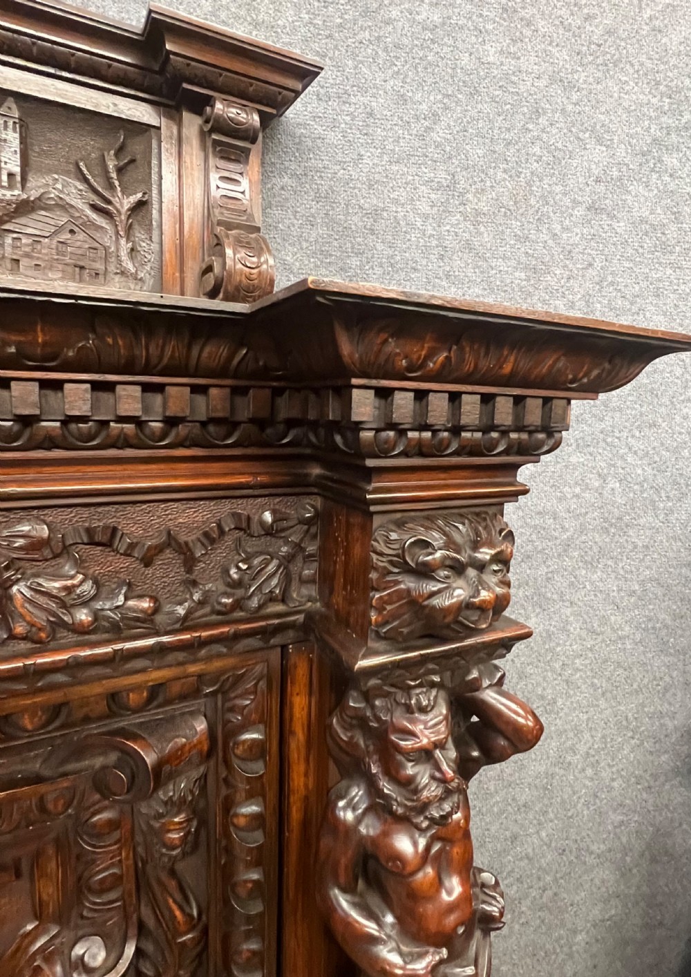A heavily carved dark walnut cabinet featuring figurative reliefs, caryatid supports, mask motifs, and an architectural cresting. View XVII