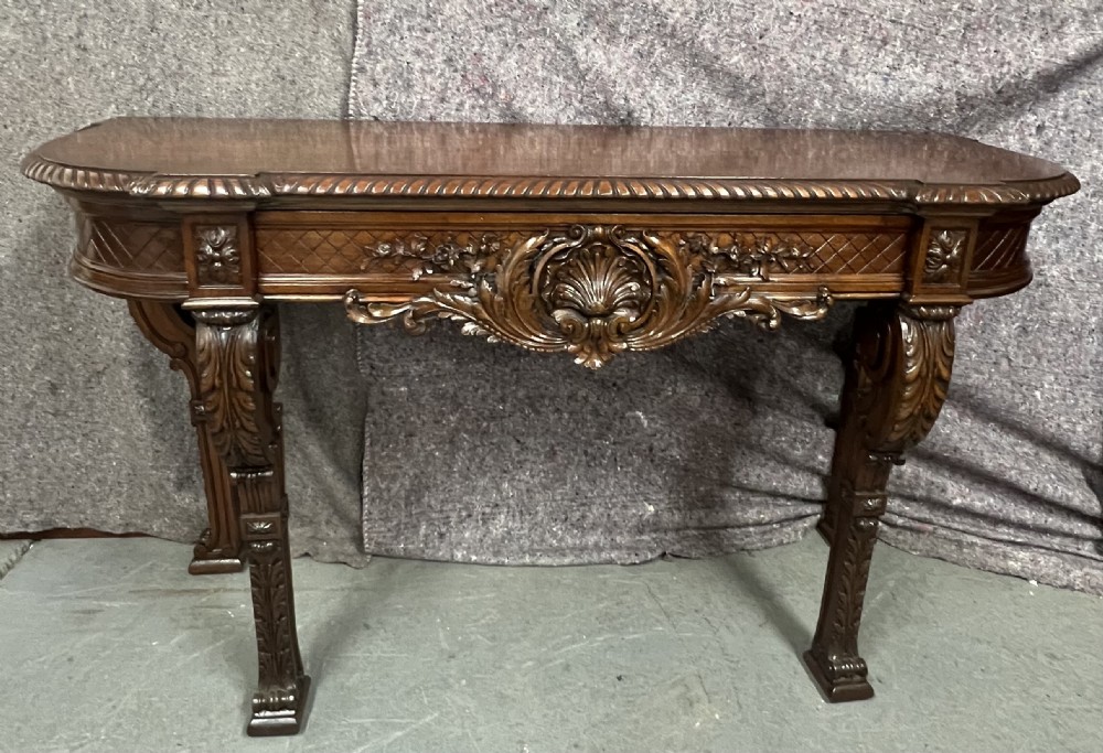 An antique dark brown carved wood console table featuring a shell motif central frieze and detailed scrolled legs.