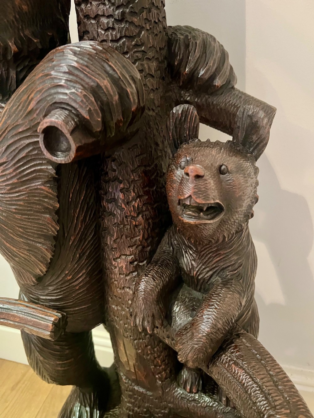 A tall dark wood hand-carved Black Forest hall stand featuring climbing bear figures, branch-form coat pegs, and an integrated umbrella ring with a drip pan base. View III