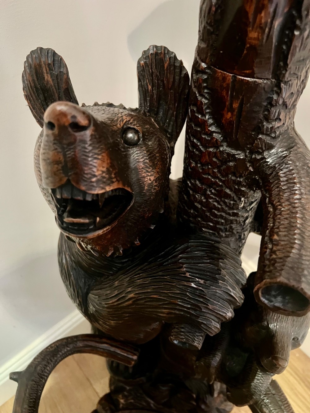 A tall dark wood hand-carved Black Forest hall stand featuring climbing bear figures, branch-form coat pegs, and an integrated umbrella ring with a drip pan base. View VI