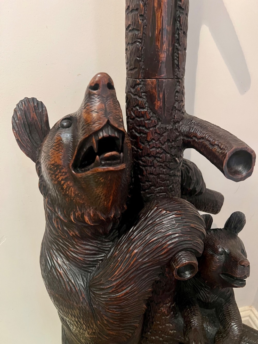 A tall dark wood hand-carved Black Forest hall stand featuring climbing bear figures, branch-form coat pegs, and an integrated umbrella ring with a drip pan base. View XV