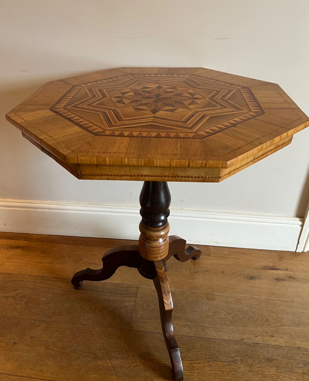 An octagonal wooden occasional table featuring geometric marquetry star patterns on the top and a turned pedestal column supported by three inlaid legs.