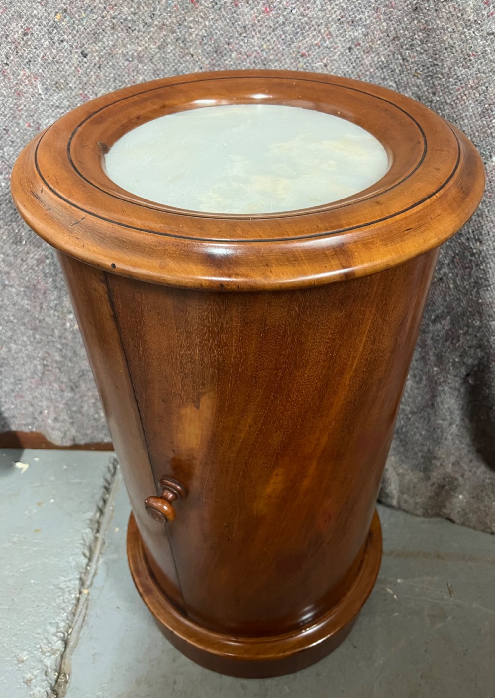 A Victorian cylindrical mahogany pedestal stand featuring an inset marble top, a curved cabinet door with a wooden turned knob, and a moulded circular base. View IV