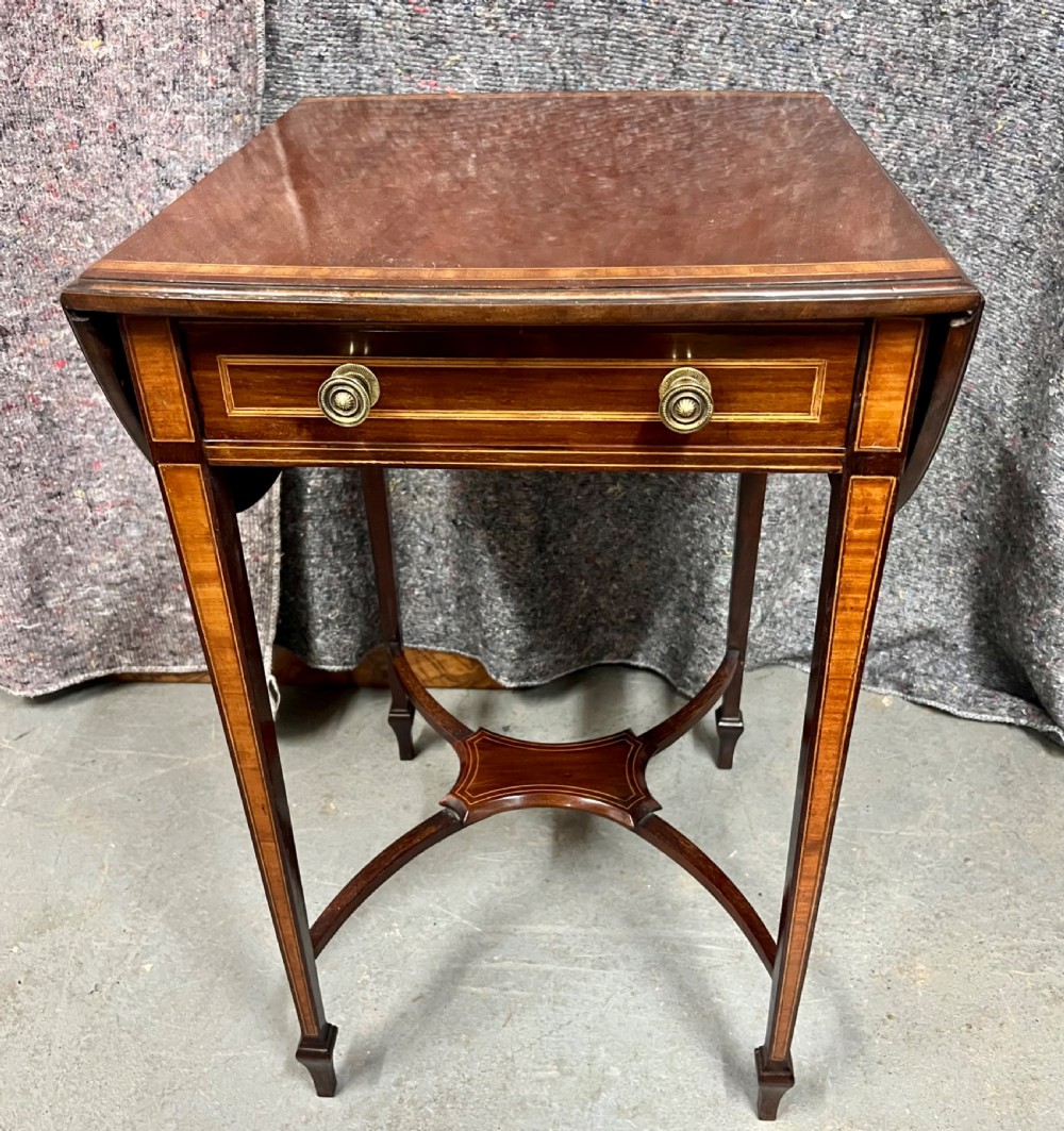 An Edwardian mahogany Pembroke side table featuring satinwood crossbanding, drop leaves, a single drawer with twin brass handles, square tapered legs, and a curved lower X-stretcher.