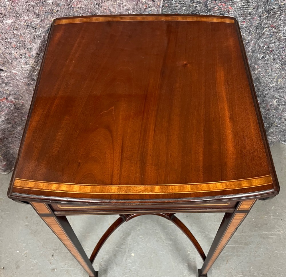 An Edwardian mahogany Pembroke side table featuring satinwood crossbanding, drop leaves, a single drawer with twin brass handles, square tapered legs, and a curved lower X-stretcher. View IV
