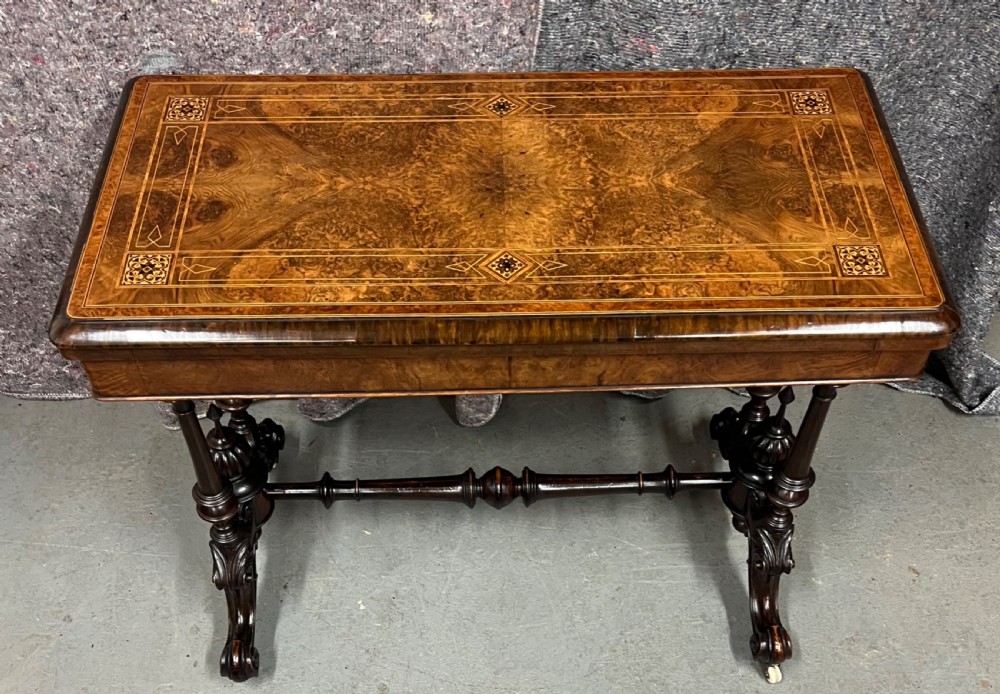 A Victorian burr walnut card table featuring geometric Tunbridge Ware inlay, turned twin-column supports, and a stretcher base on castors.