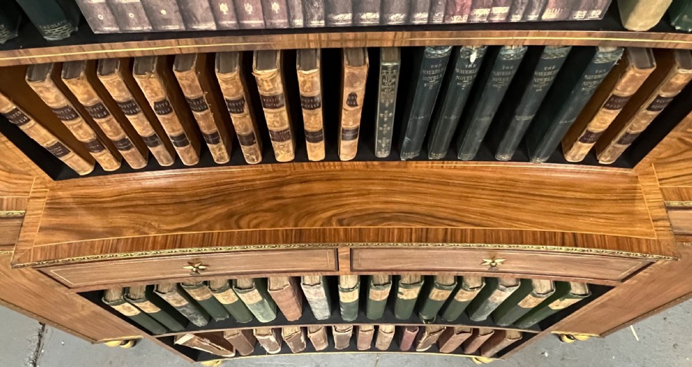 A Regency style rosewood breakfront open bookcase with tiered shelving filled with books, brass star handles, mirrored side compartments, and turned legs. View XVI