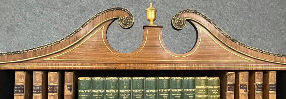 A Regency style rosewood breakfront open bookcase with tiered shelving filled with books, brass star handles, mirrored side compartments, and turned legs. View XVII