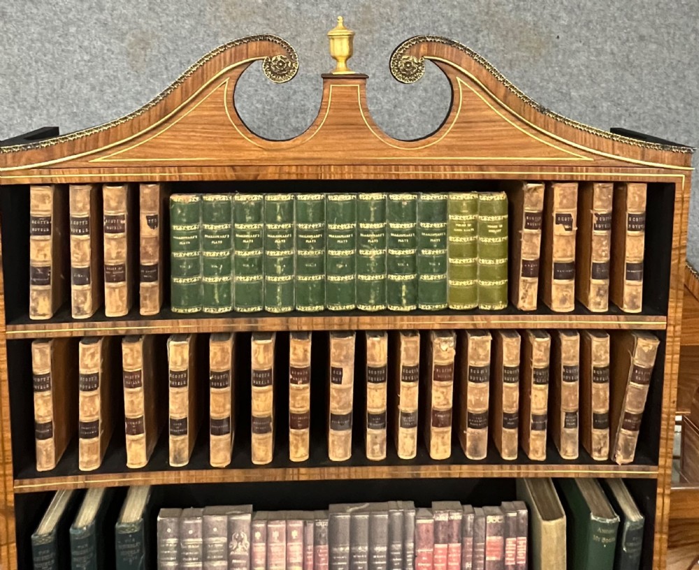 A Regency style rosewood breakfront open bookcase with tiered shelving filled with books, brass star handles, mirrored side compartments, and turned legs. View XVIII
