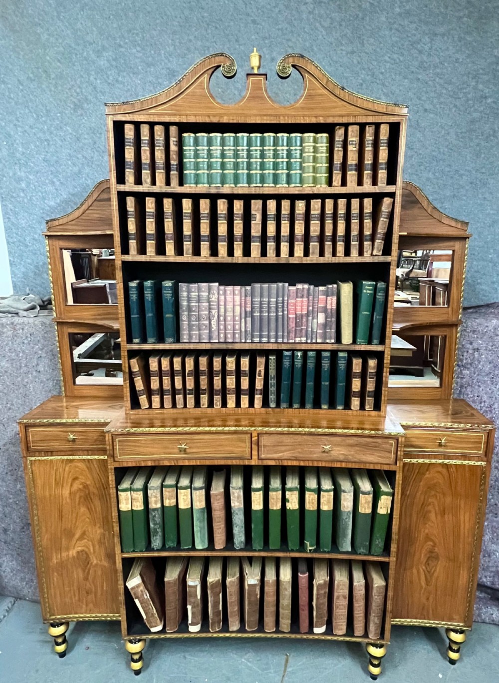 A Regency style rosewood breakfront open bookcase with tiered shelving filled with books, brass star handles, mirrored side compartments, and turned legs. View XIX