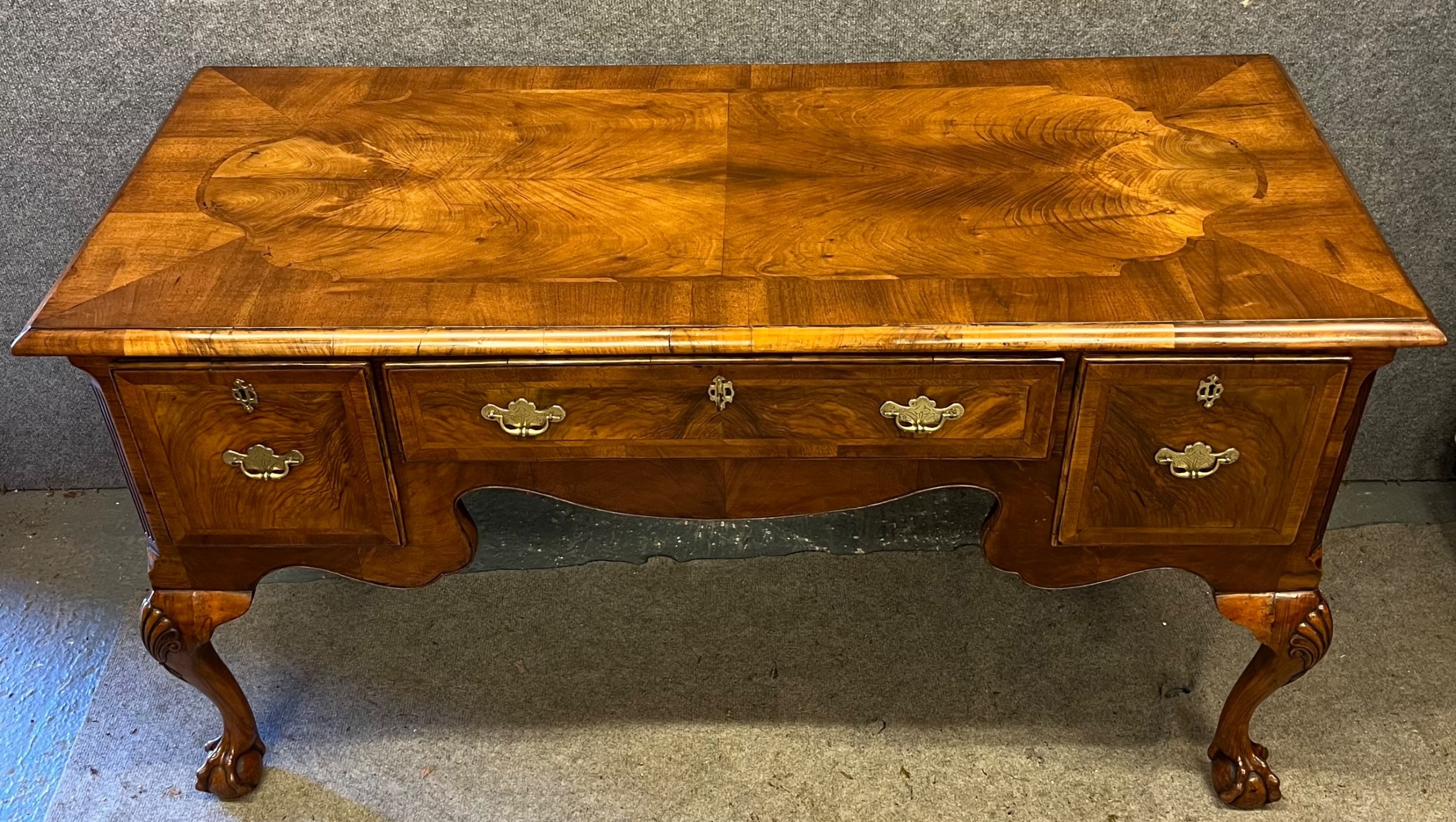 An antique walnut writing desk featuring three drawers, crossbanded veneer top, carved cabriole legs, and claw and ball feet.