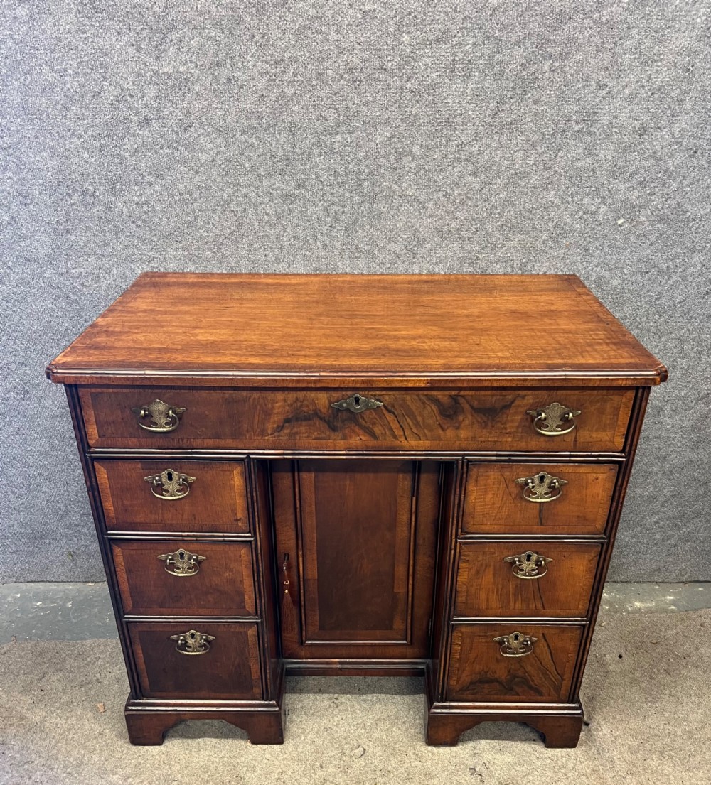 An 18th-century style walnut kneehole desk featuring a top drawer, six pedestal drawers with brass drop handles, a central recessed cupboard, and bracket feet.