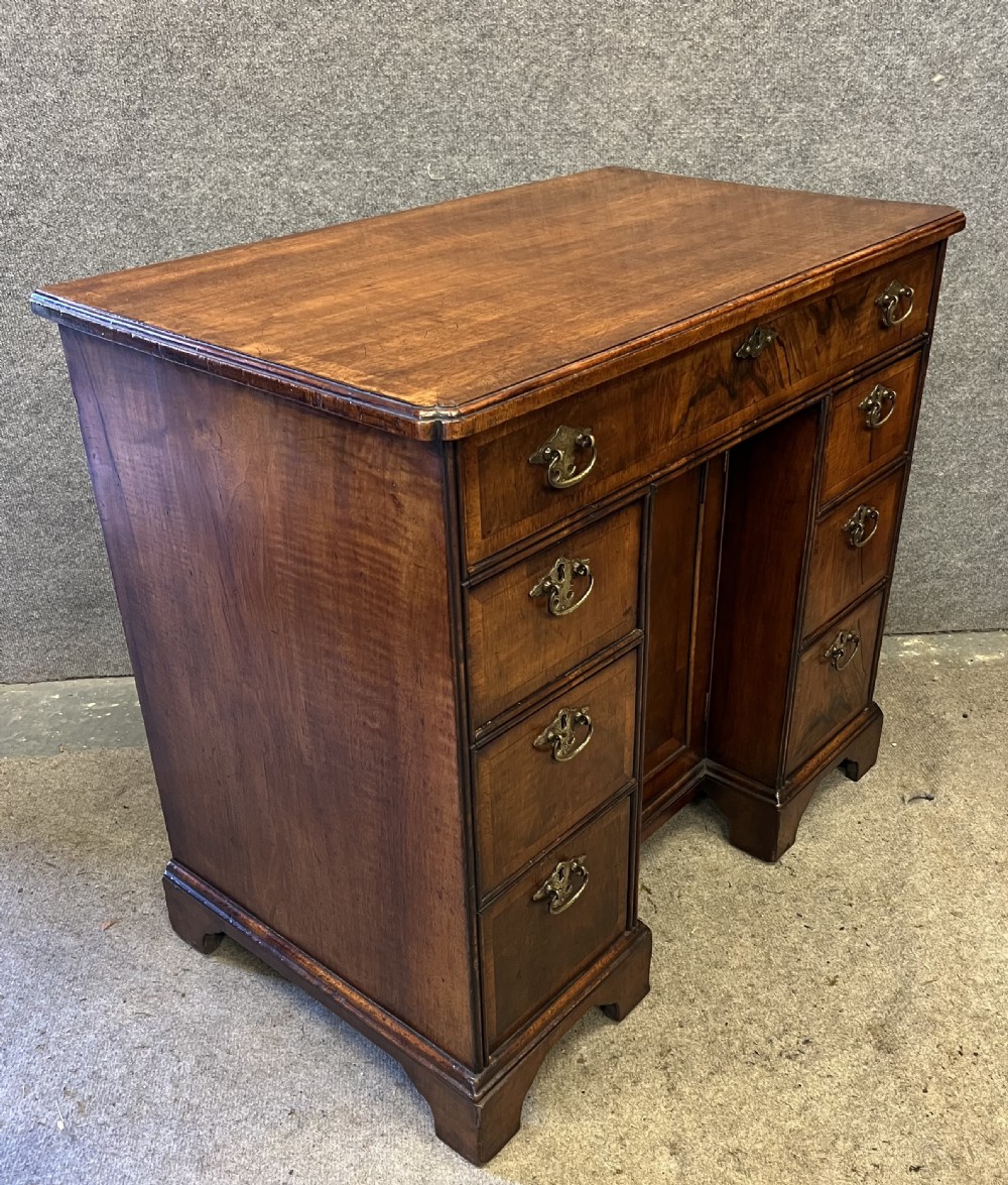 An 18th-century style walnut kneehole desk featuring a top drawer, six pedestal drawers with brass drop handles, a central recessed cupboard, and bracket feet. View II