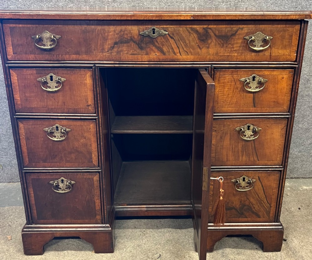 An 18th-century style walnut kneehole desk featuring a top drawer, six pedestal drawers with brass drop handles, a central recessed cupboard, and bracket feet. View VIII