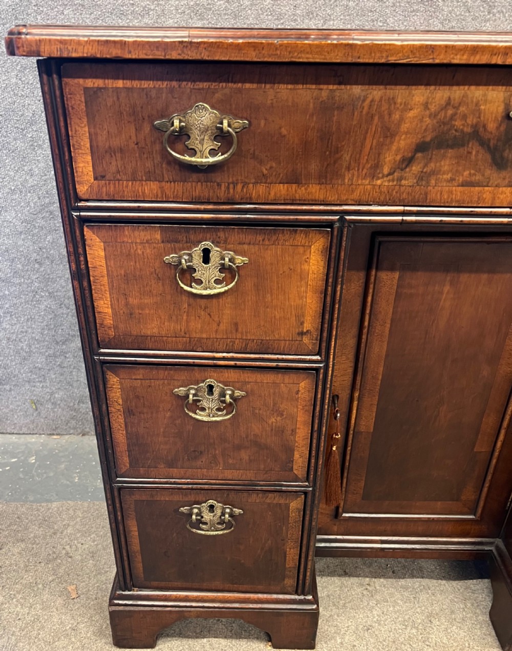 An 18th-century style walnut kneehole desk featuring a top drawer, six pedestal drawers with brass drop handles, a central recessed cupboard, and bracket feet. View IX