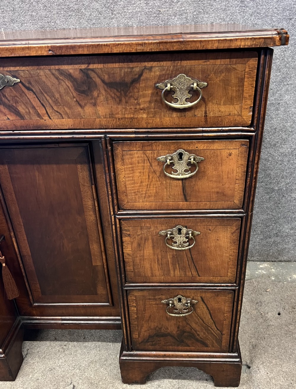 An 18th-century style walnut kneehole desk featuring a top drawer, six pedestal drawers with brass drop handles, a central recessed cupboard, and bracket feet. View X