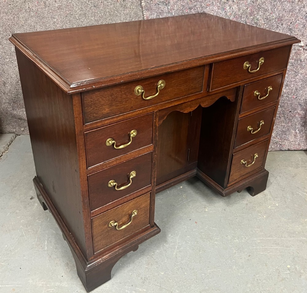 A George III mahogany kneehole desk featuring multiple drawers with brass swan-neck handles, a central recessed cupboard, and bracket feet.
