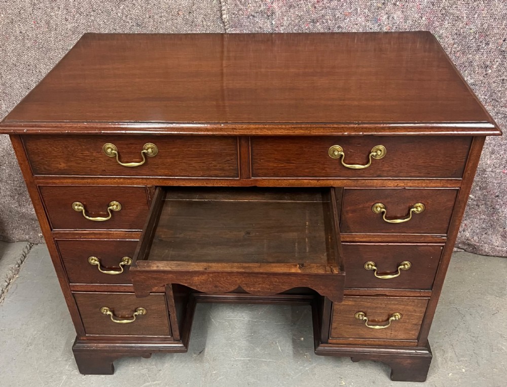 A George III mahogany kneehole desk featuring multiple drawers with brass swan-neck handles, a central recessed cupboard, and bracket feet. View VI