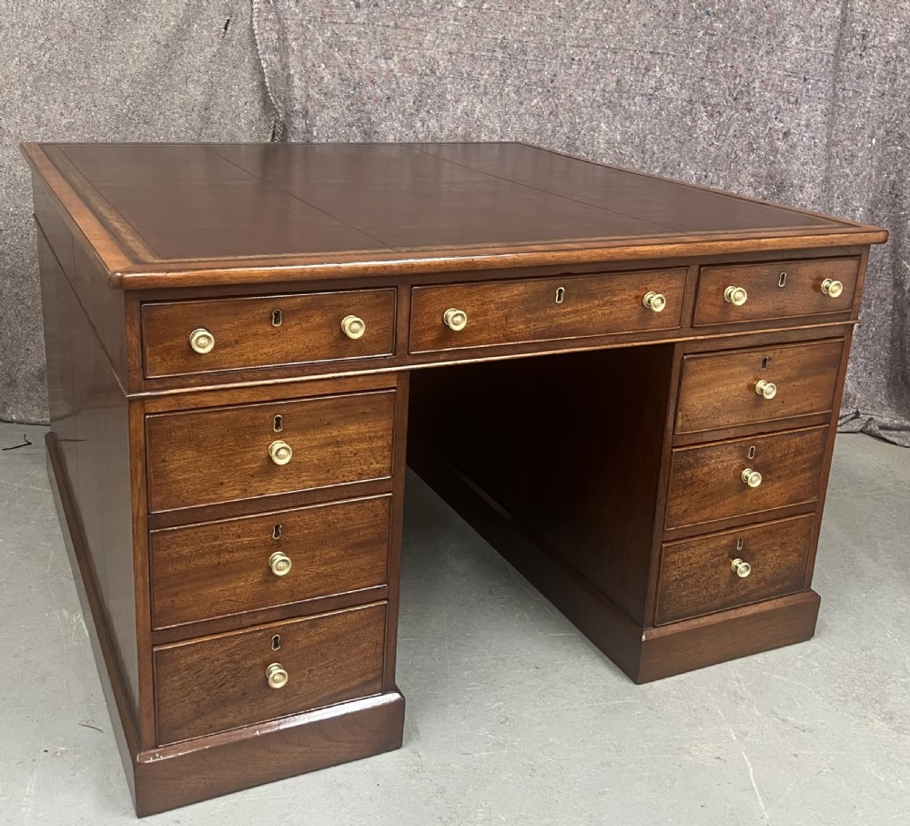 A George III mahogany partners desk featuring a leather writing surface, multiple drawers with turned brass handles, and a twin-pedestal design.