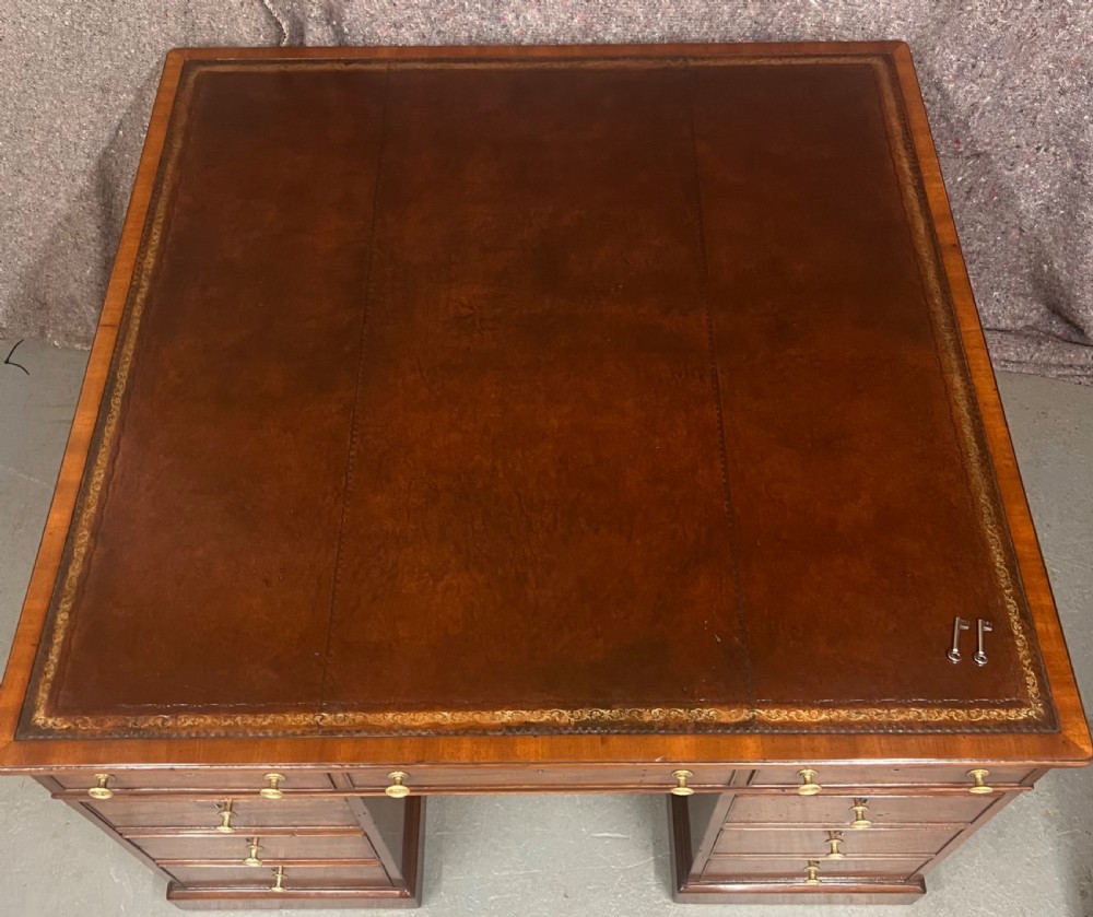 A George III mahogany partners desk featuring a leather writing surface, multiple drawers with turned brass handles, and a twin-pedestal design. View IX