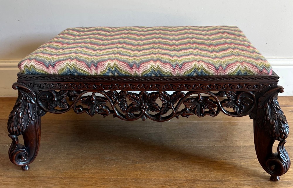 A large rectangular Anglo-Indian stool featuring an intricately carved dark hardwood apron and cabriole legs, topped with a flame-stitch patterned tapestry cushion. View II