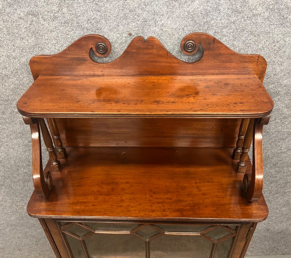 A small Regency mahogany cabinet featuring an upper scroll gallery, turned spindle supports, and a single glazed door with geometric timber tracery. View V