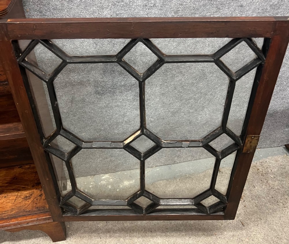 A small Regency mahogany cabinet featuring an upper scroll gallery, turned spindle supports, and a single glazed door with geometric timber tracery. View X