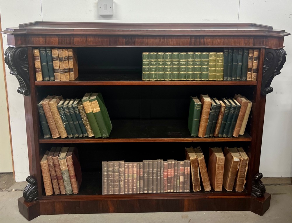 An antique dark rosewood open bookcase featuring three wide shelves, rich figured grain, and hand-carved decorative corbels on the upper front corners.