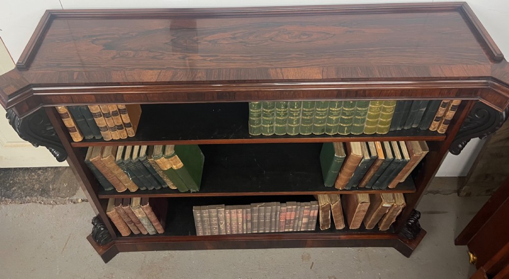 An antique dark rosewood open bookcase featuring three wide shelves, rich figured grain, and hand-carved decorative corbels on the upper front corners. View II