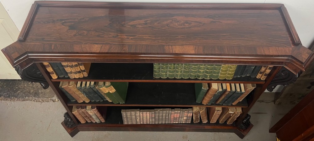 An antique dark rosewood open bookcase featuring three wide shelves, rich figured grain, and hand-carved decorative corbels on the upper front corners. View VII
