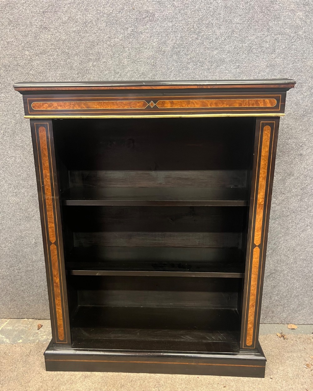 A small ebonised open bookcase with three shelves, featuring burr walnut inlay banding and thin brass moulding detailing. View II