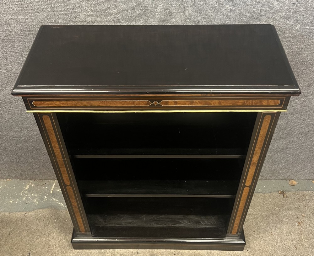 A small ebonised open bookcase with three shelves, featuring burr walnut inlay banding and thin brass moulding detailing. View XII