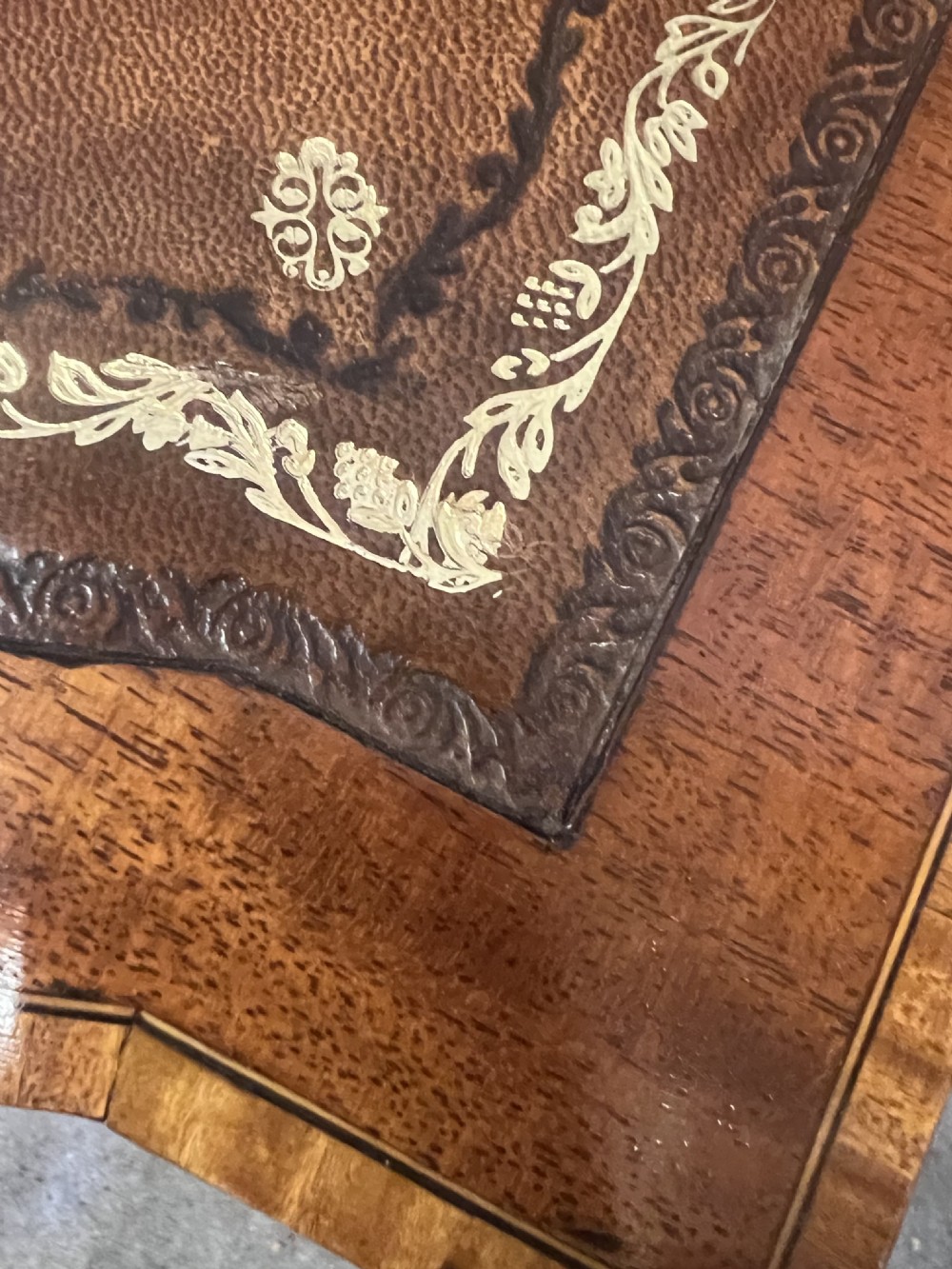 An Edwardian inlaid mahogany writing desk featuring a leather-lined top, a curved serpentine front, seven drawers with brass drop handles, and tapered square legs on castors. View V
