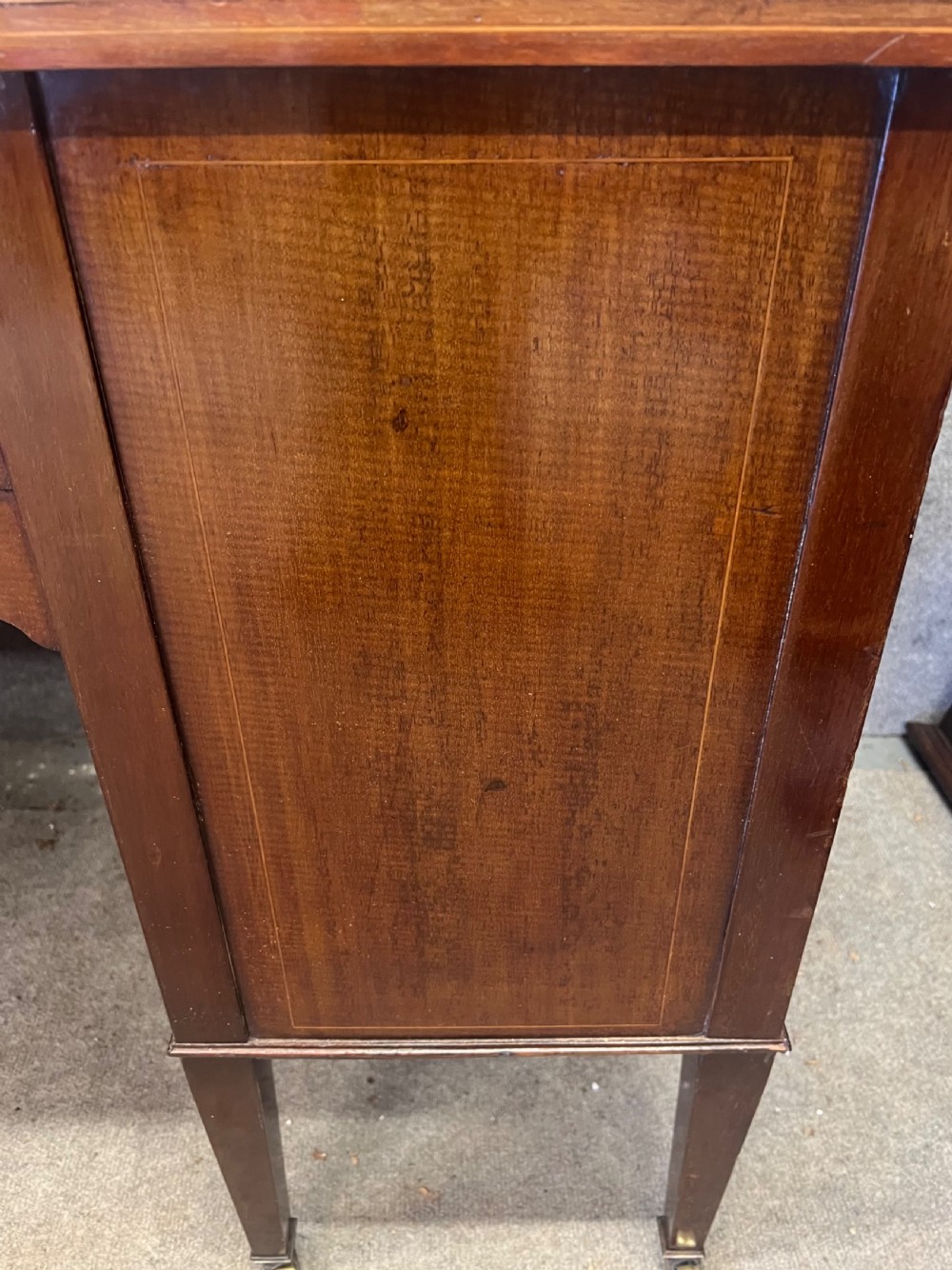 An Edwardian inlaid mahogany writing desk featuring a leather-lined top, a curved serpentine front, seven drawers with brass drop handles, and tapered square legs on castors. View XII