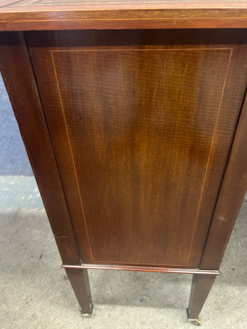 An Edwardian inlaid mahogany writing desk featuring a leather-lined top, a curved serpentine front, seven drawers with brass drop handles, and tapered square legs on castors. View XIII