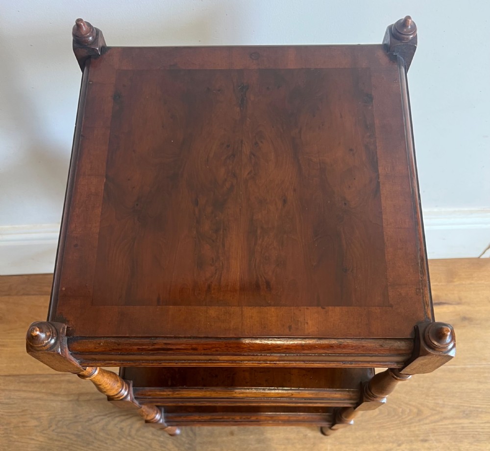 A three-tier dark mahogany antique whatnot featuring turned upright supports, top corner finials, and small brass castors on the legs. View IV