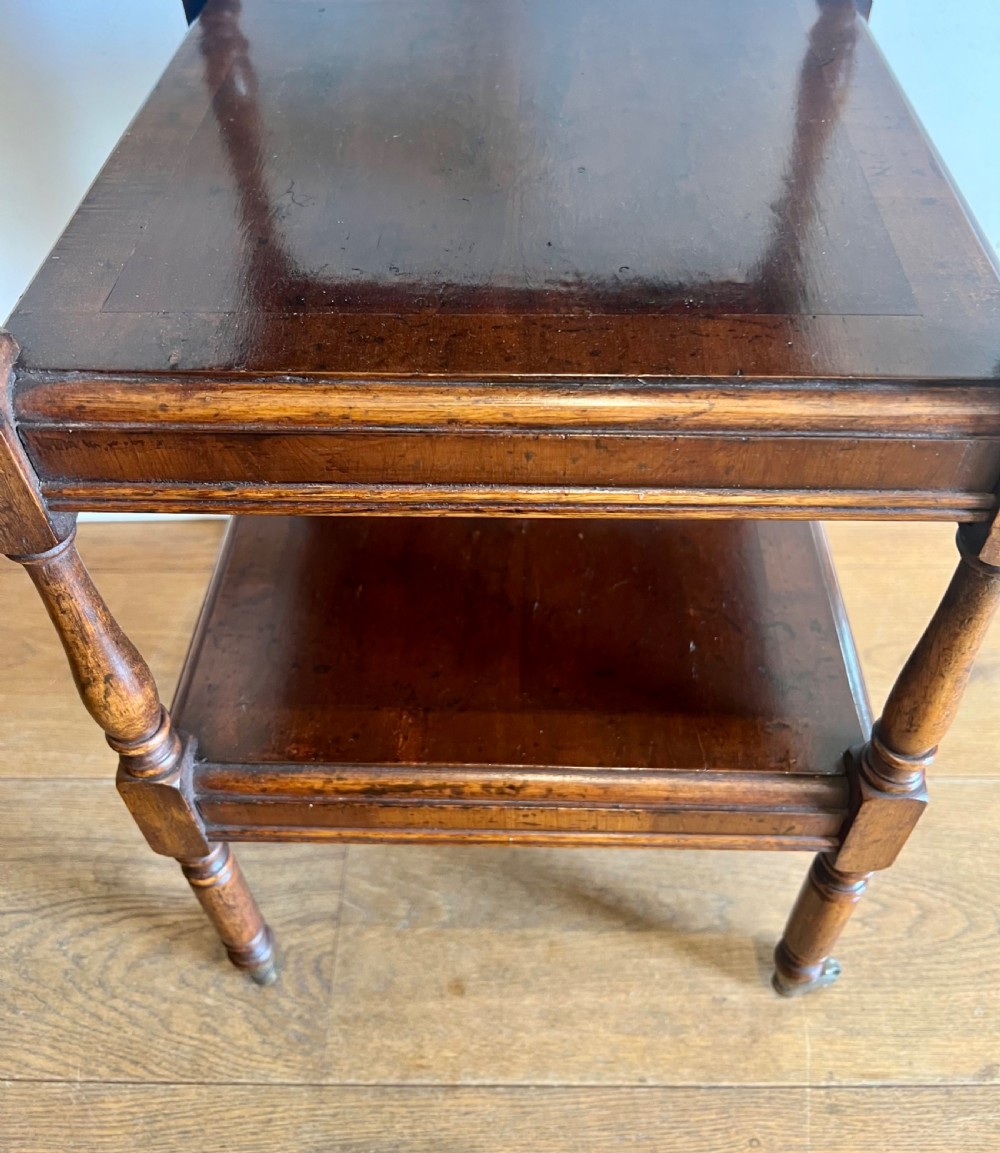 A three-tier dark mahogany antique whatnot featuring turned upright supports, top corner finials, and small brass castors on the legs. View V