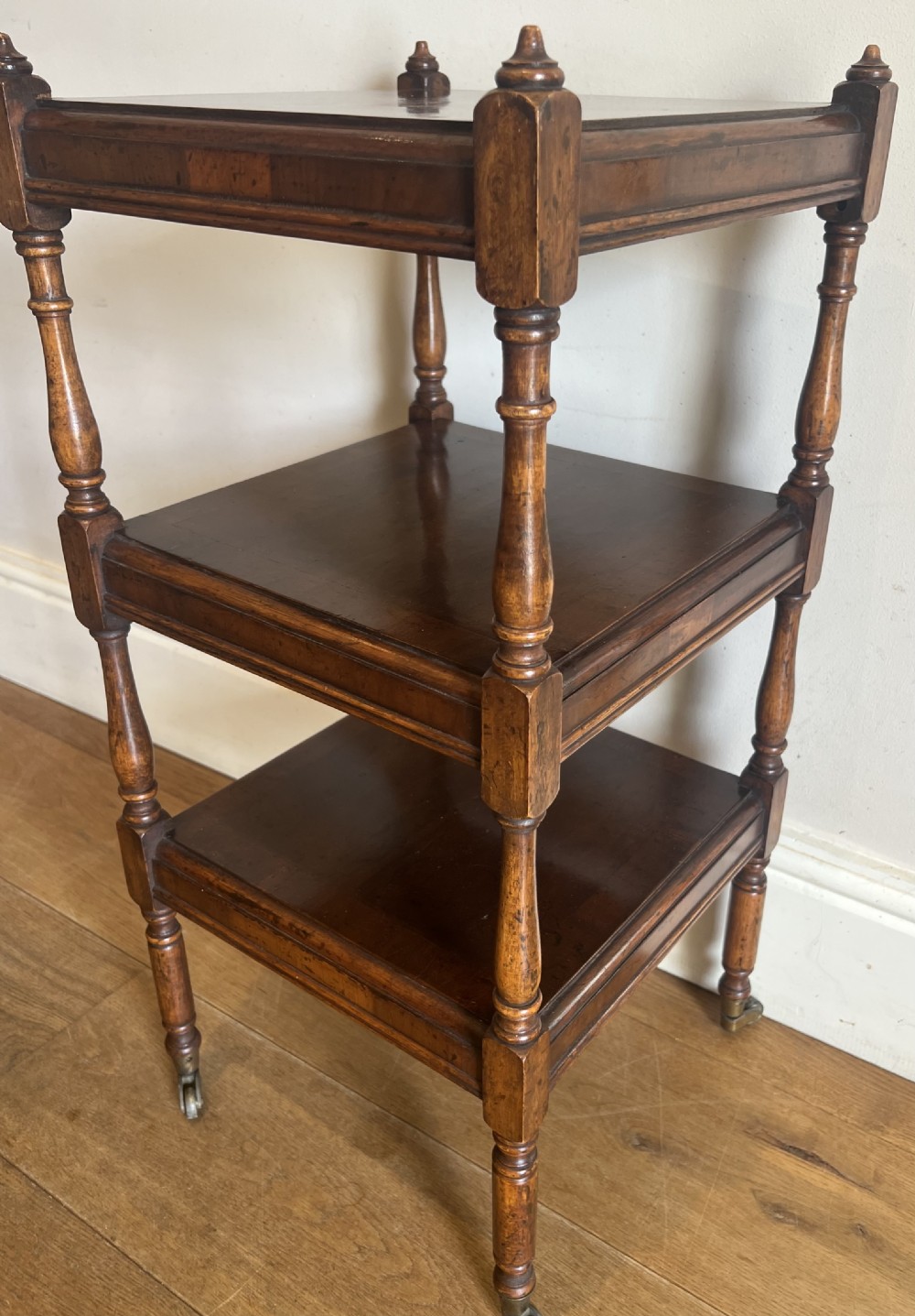A three-tier dark mahogany antique whatnot featuring turned upright supports, top corner finials, and small brass castors on the legs. View VIII