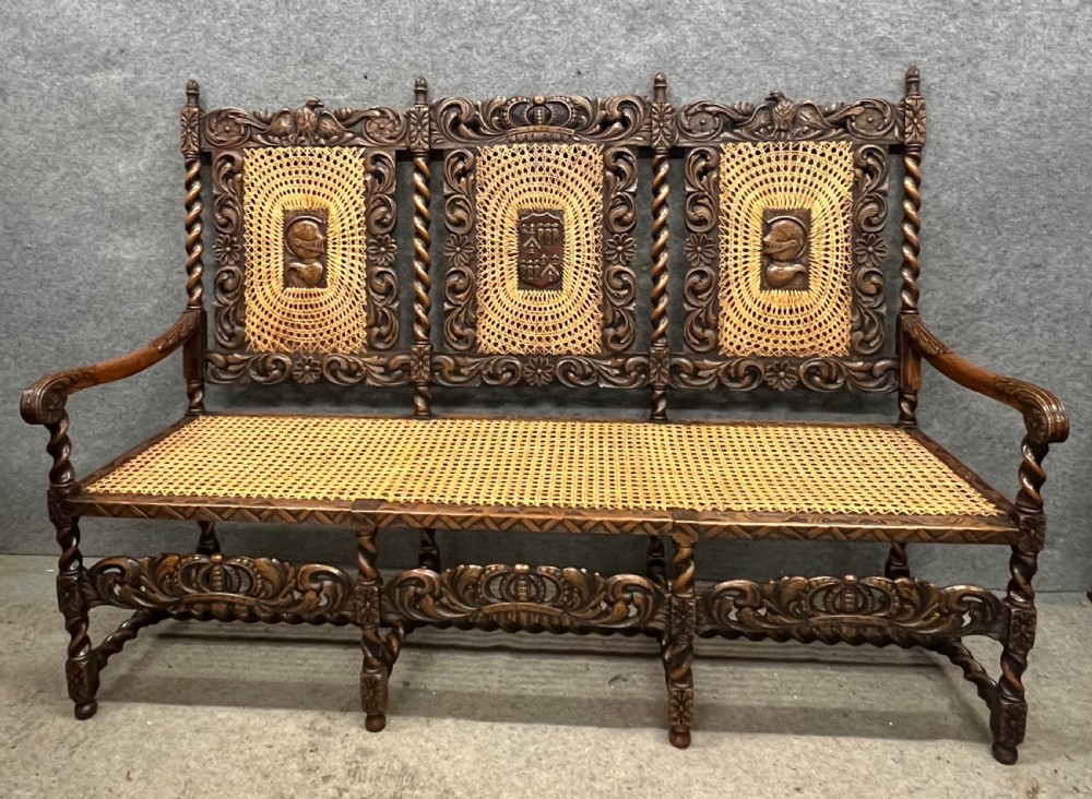 A carved dark wood Carolean style triple chair-back settee with barley twist turnings, crest carving, and woven cane seat and back panels.