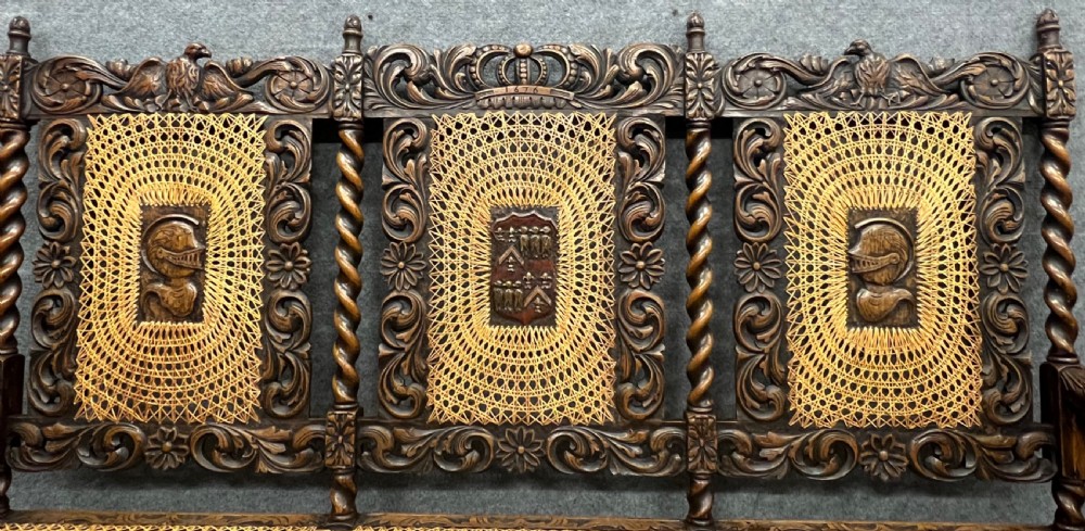 A carved dark wood Carolean style triple chair-back settee with barley twist turnings, crest carving, and woven cane seat and back panels. View X