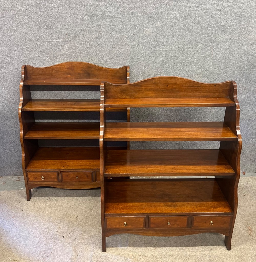 A pair of rich brown mahogany open waterfall bookcases featuring graduated shelves, serpentine side profiles, and three small drawers along the base.