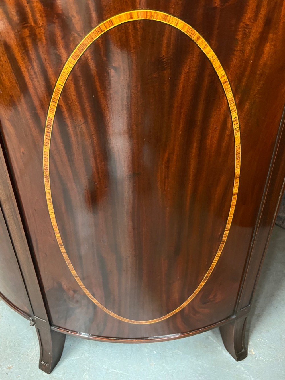 A semi-circular Sheraton Revival mahogany cabinet featuring decorative oval wood inlays, stringing details, and square tapered legs. View III