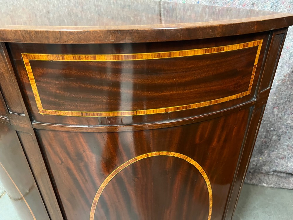 A semi-circular Sheraton Revival mahogany cabinet featuring decorative oval wood inlays, stringing details, and square tapered legs. View IV