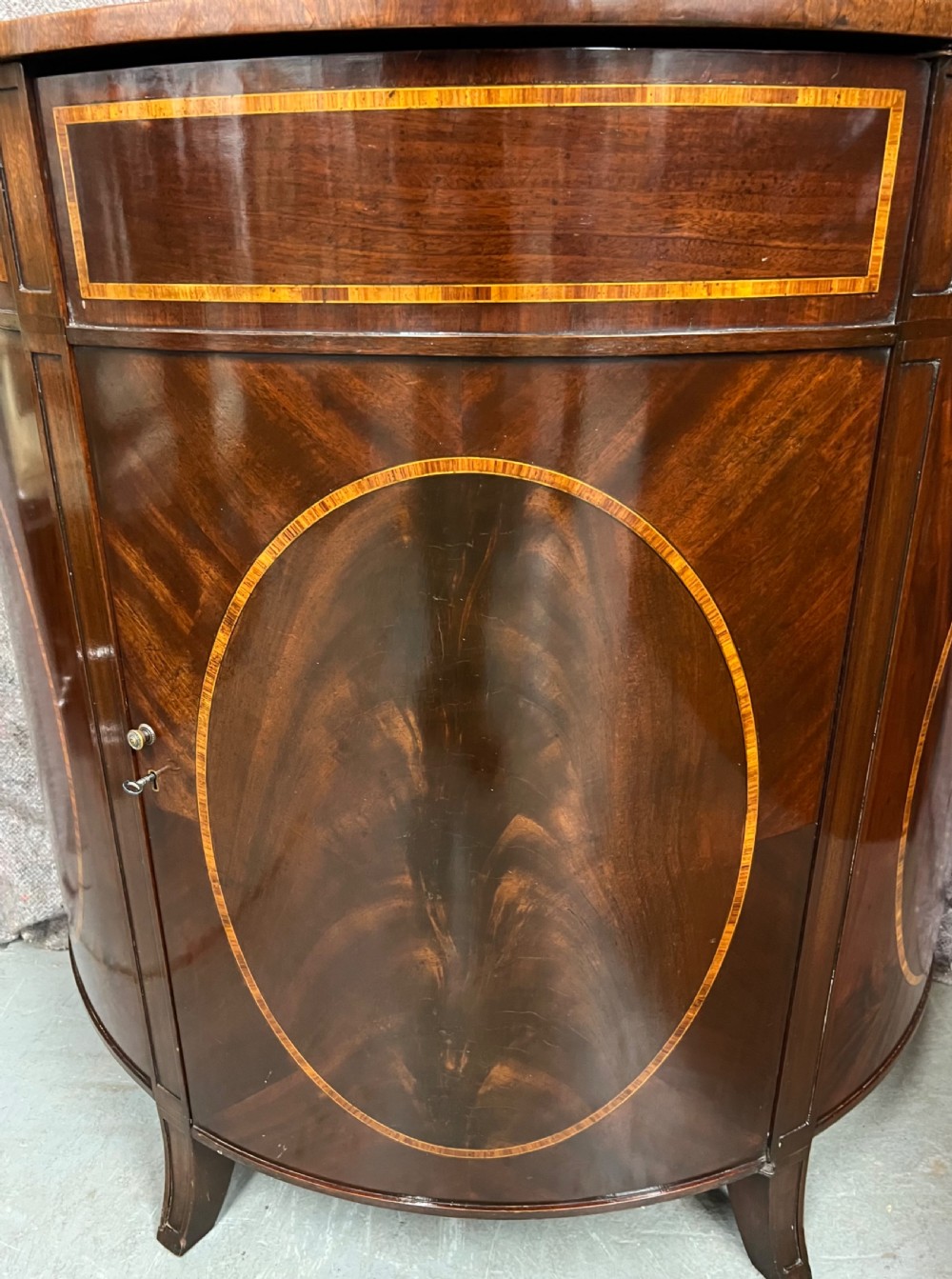 A semi-circular Sheraton Revival mahogany cabinet featuring decorative oval wood inlays, stringing details, and square tapered legs. View VI