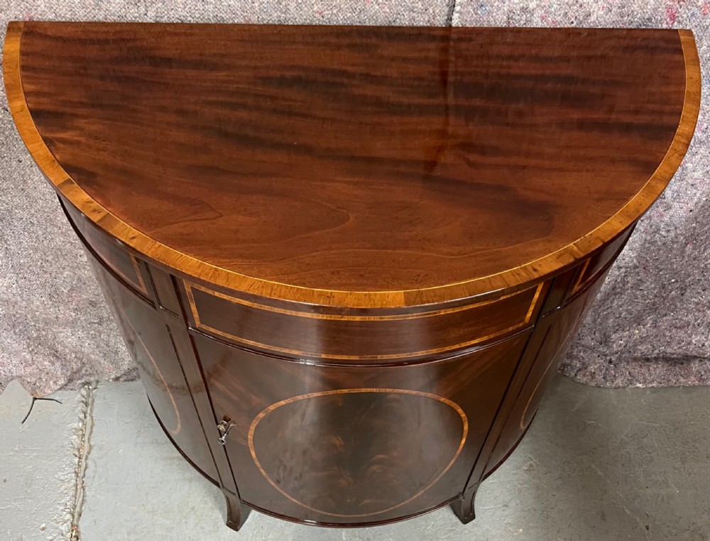 A semi-circular Sheraton Revival mahogany cabinet featuring decorative oval wood inlays, stringing details, and square tapered legs. View VIII