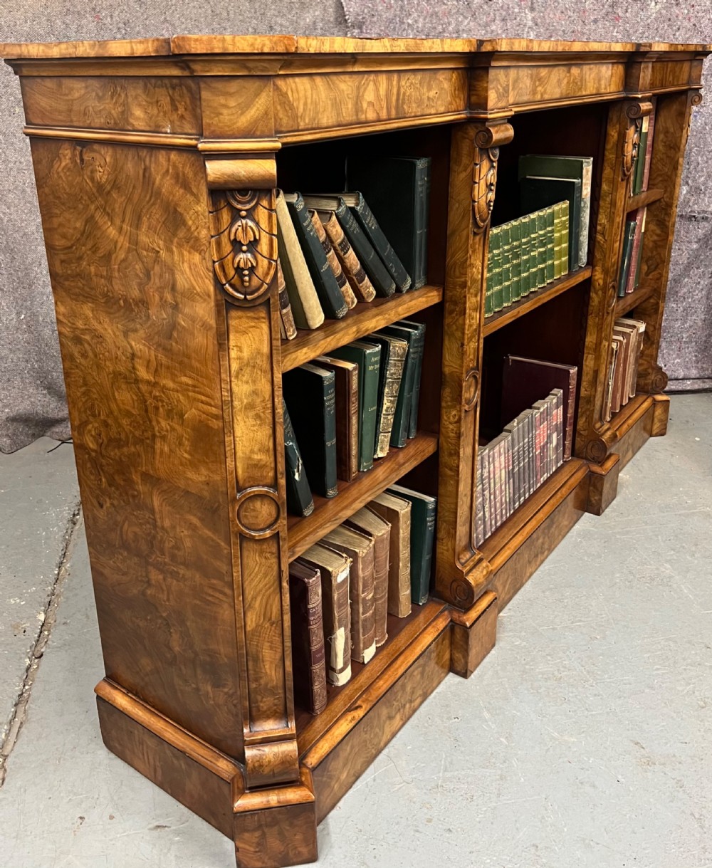 A low, wide Victorian burr walnut open bookcase with three compartmentalised shelf sections, carved pilaster corbels, and a solid plinth base. View II